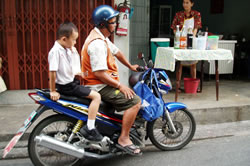 バイクタクシーに乗って帰宅する子ども。手には清涼飲料水の入ったビニール袋が。